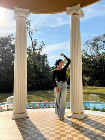 Julie posando entre unas columnas de estilo gregoriano, con un jardín de fondo.